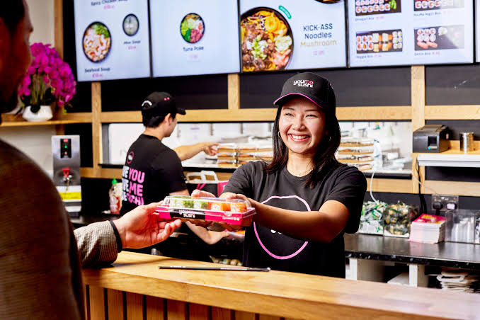 YouMeSushi team member handing a fresh sushi box to a customer